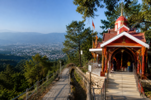 सन्तला देवी मंदिर देहरादून: इतिहास, ट्रेक, दर्शन समय और यात्रा गाइड की पूरी जानकारी 2 देहरादून की हरी-भरी पहाड़ियों के बीच स्थित सन्तला देवी मंदिर का मनोरम दृश्य, जहां मंदिर तक जाने वाला पैदल मार्ग और नीचे फैली दून घाटी दिखाई दे रही है।